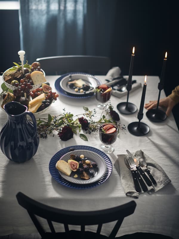 Table élégamment dressée avec un pichet VANLIGEN et des couverts LIVNÄRA sur une nappe blanche, dans une pièce sombre.