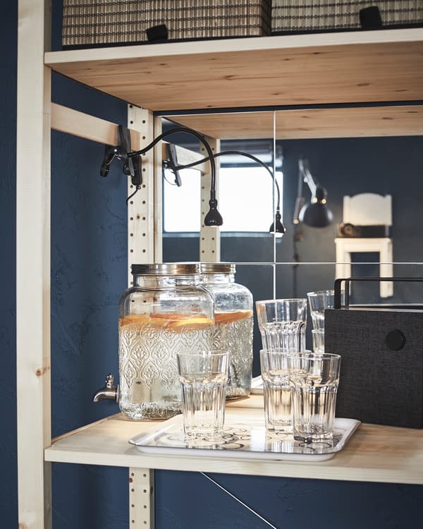 Tablette d’étagère servant de mini bar: fontaine à eau remplie, un plateau de verres, une enceinte Bluetooth.