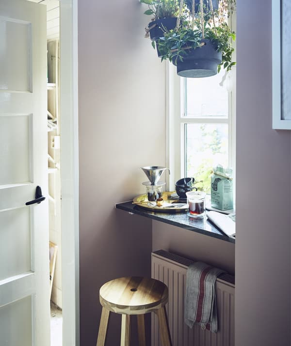 Tabouret et rebord devant une grande fenêtre, avec plantes suspendues et coin pour préparer le café
