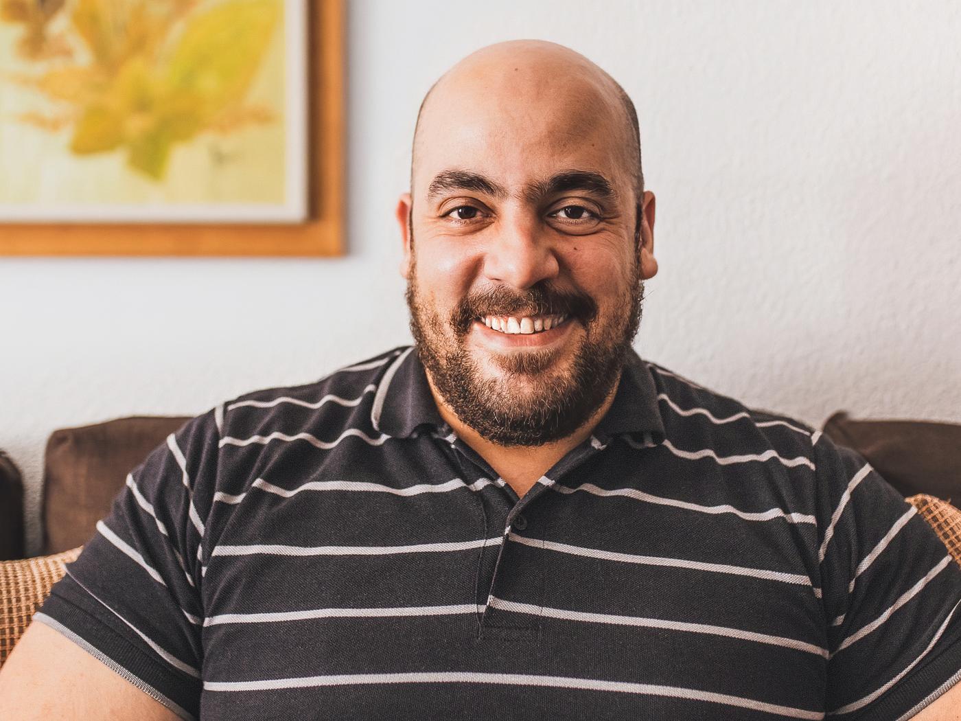 Tarek, a Syrian refugee and IKEA Spain co-worker, smiling, wearing a brown and white striped shirt.