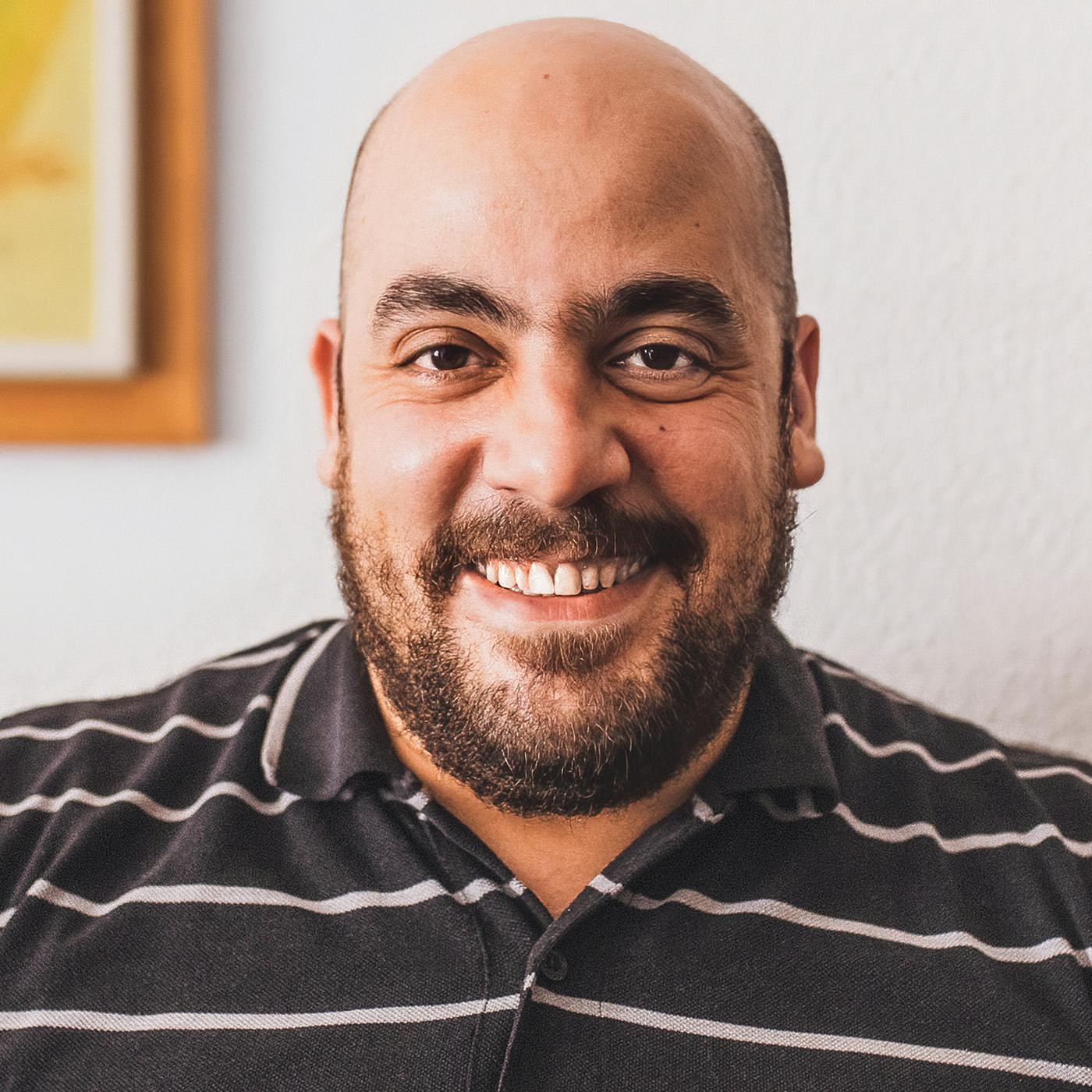 Tarek, a Syrian refugee and IKEA Spain co-worker, smiling, wearing a brown and white striped shirt.