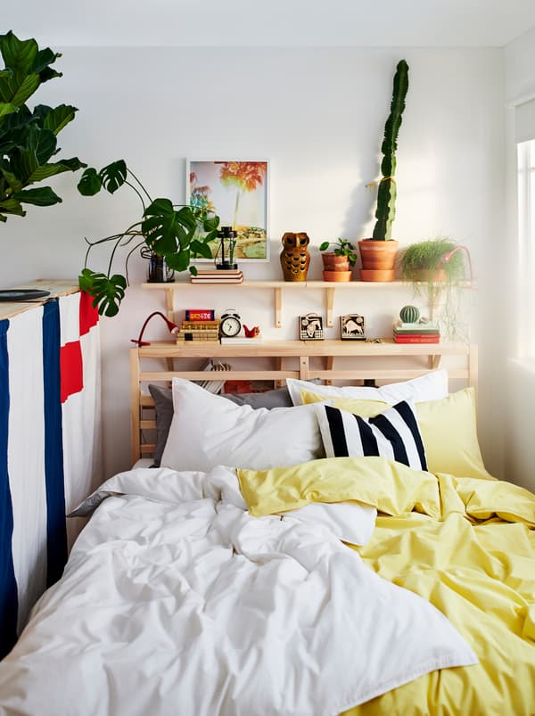 TARVA bed with two sets of ÄNGSLILJA bed linen, one yellow and one white. Plants and decorations on a shelf above the bed.