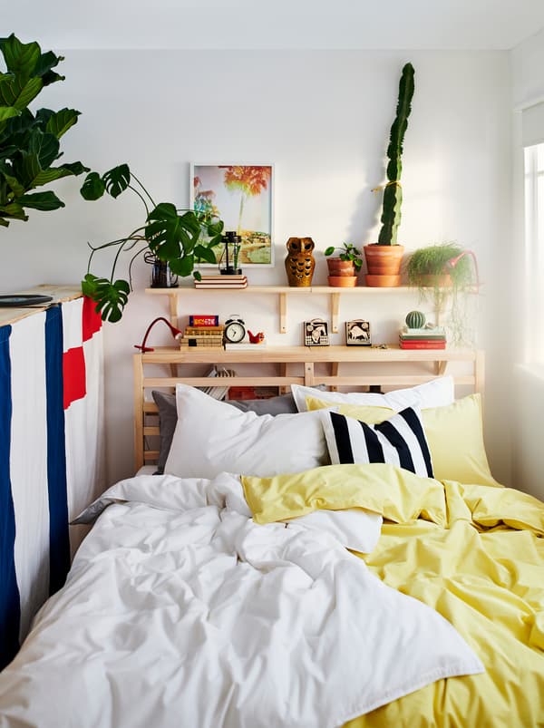 TARVA bed with two sets of ÄNGSLILJA bed linen, one yellow and one white. Plants and decorations on a shelf above the bed.