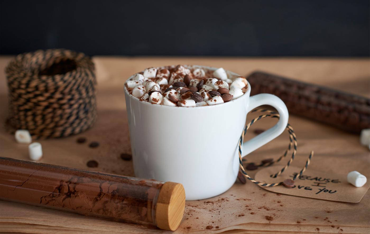 Tasse blanche remplie de chocolat chaud, garni de copeaux de chocolat et de mini-marshmallows.