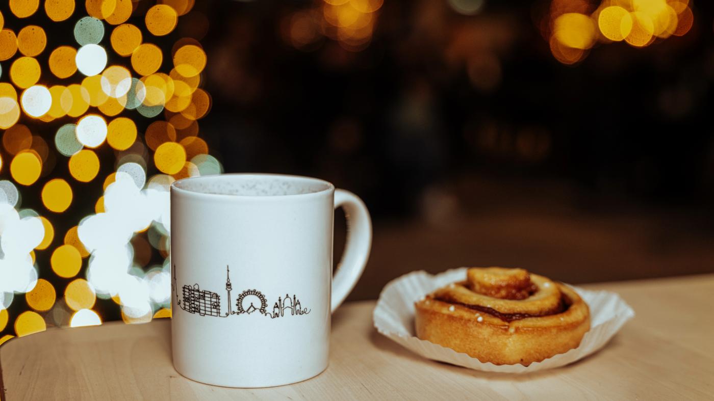 Tasse mit Heißgetränk und schwedische Zimtschnecke auf einem Holztisch.