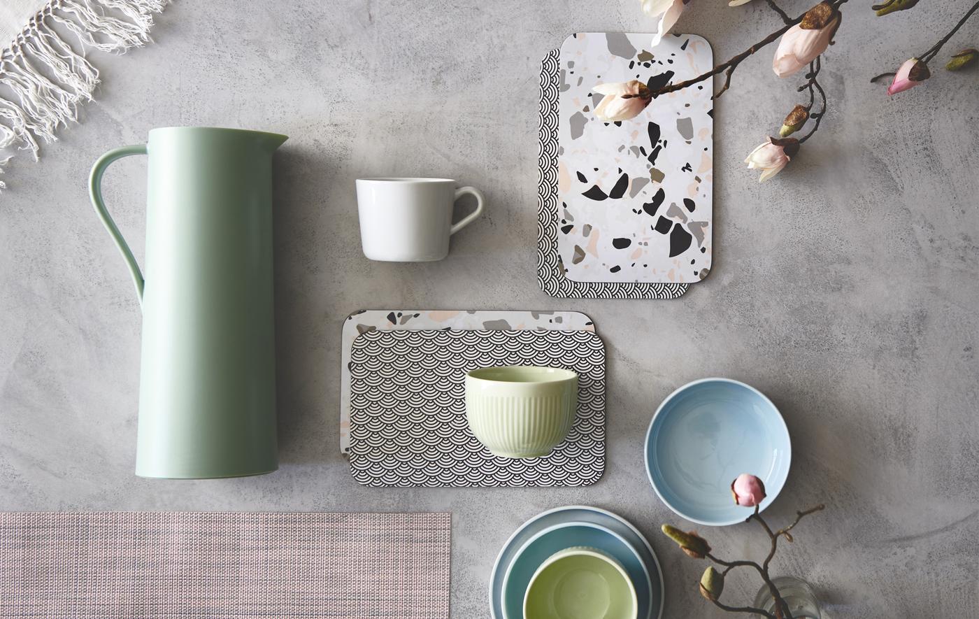 Tasses et plateaux dans des coloris pastels, posés sur une surface en béton.