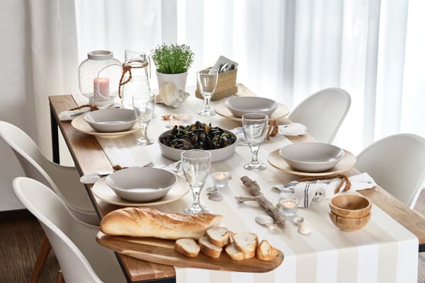Tavola estiva con conchiglie, pane, candele, bicchieri e ciotole nei toni chiari e naturali.