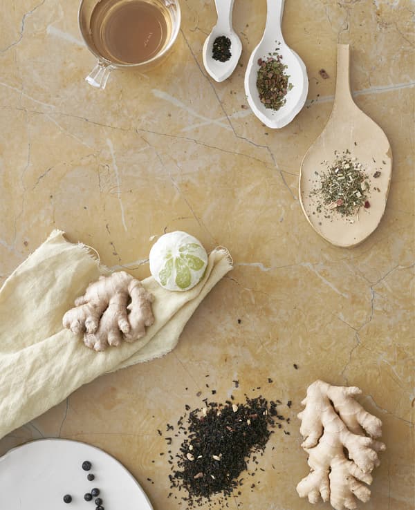Tea leaves in ceramic spoons, ginger root and a lime.