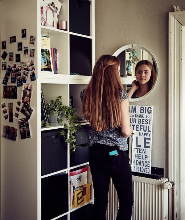 Teenager Malin looking in the mirror next to a cubed storage unit.