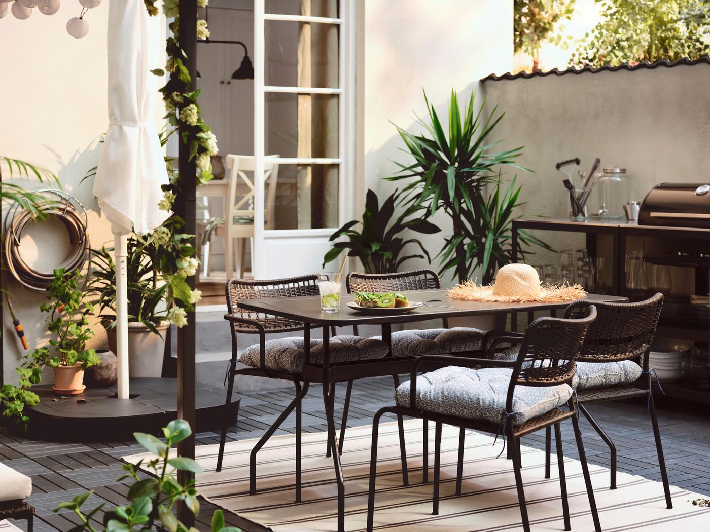 Terrasse avec table VIHOLMEN entourée de quatre chaises LÄCKÖ, et cuisine d’extérieur GRILLSKÄR avec barbecue à charbon de bois.