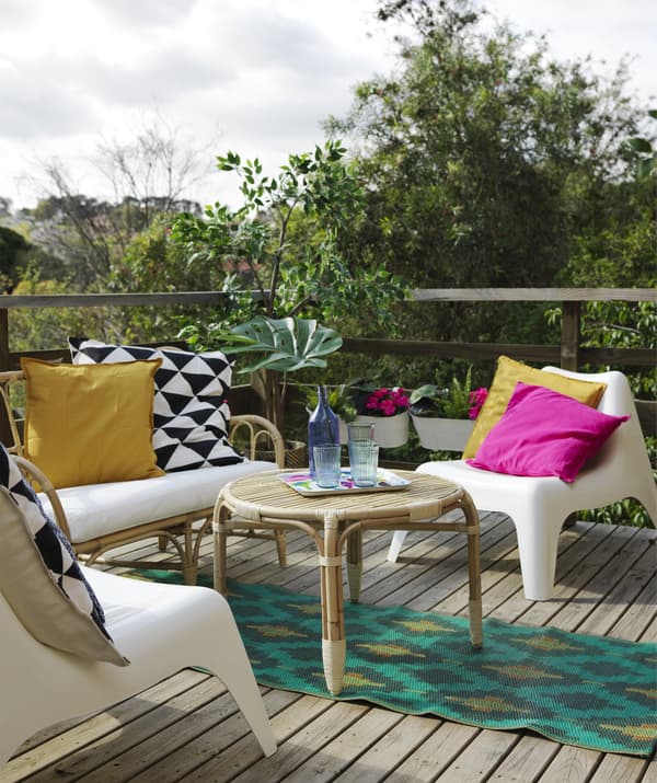 Terrasse avec un canapé et une table en rotin, des fauteuils en plastique et un tapis et des coussins colorés.