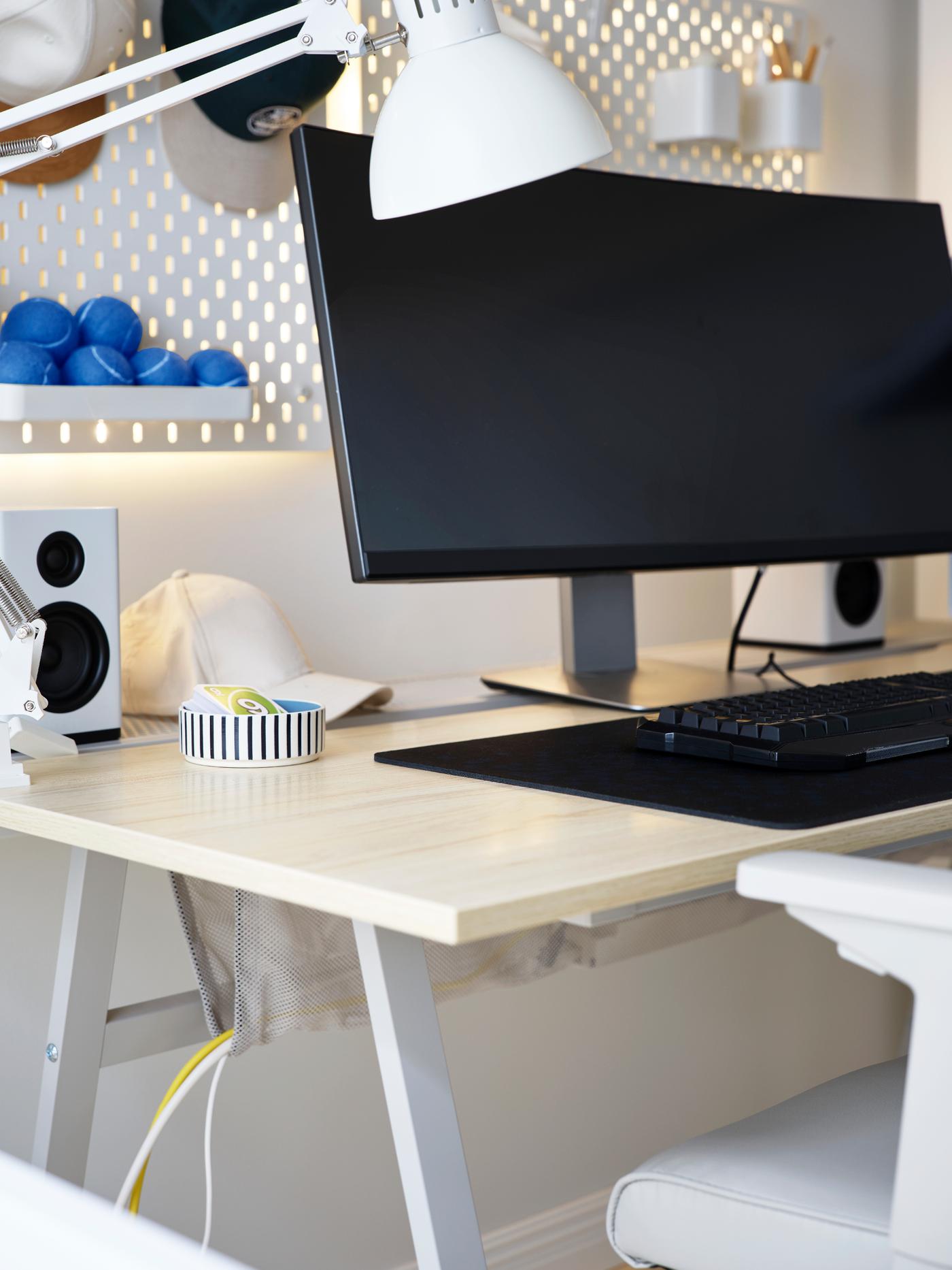 The ash effect top and grey legs of an UTESPELARE gaming desk seen from a corner. Cables hang in the attached net bag below.