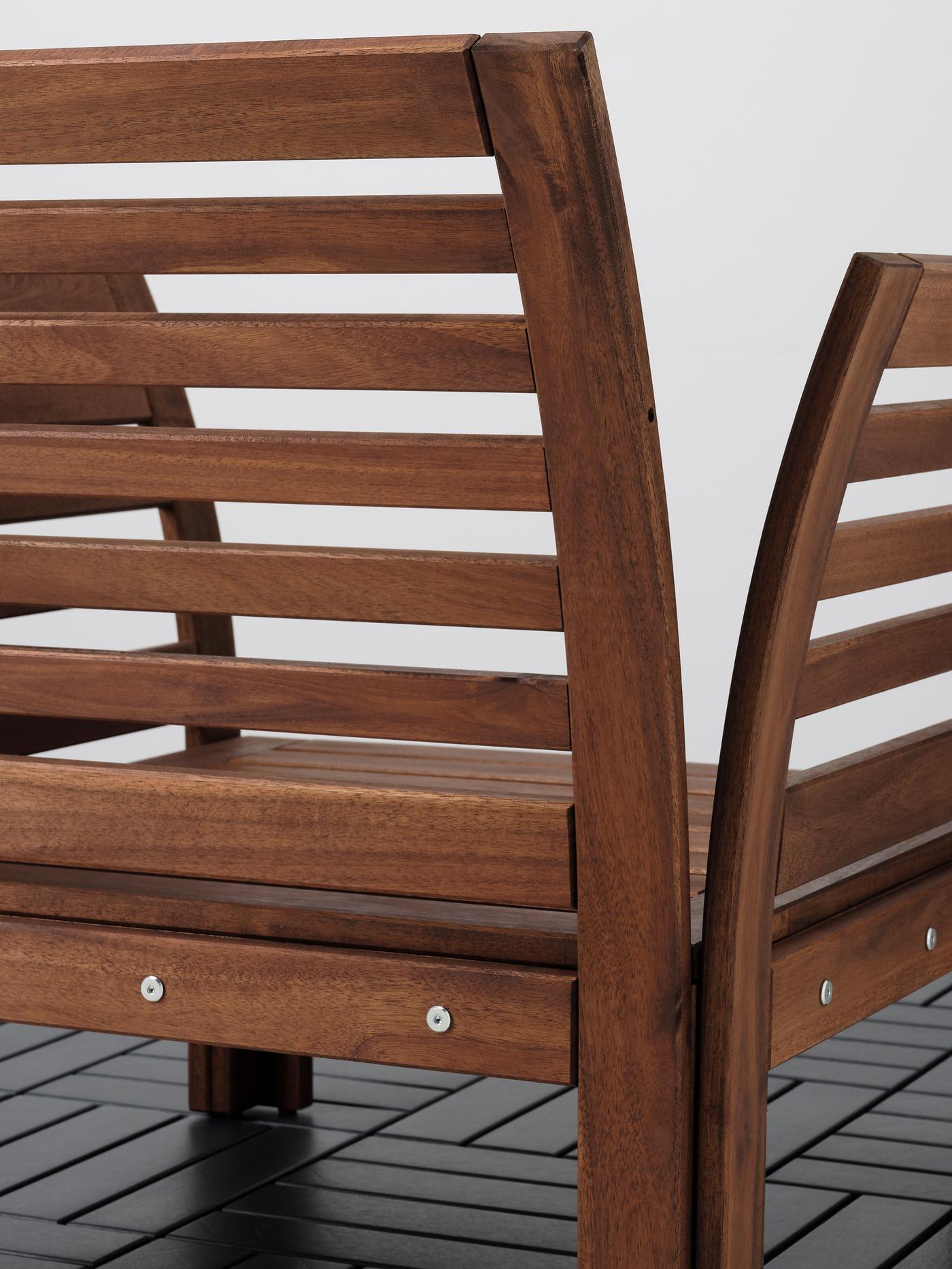 The back side of an ÄPPLARÖ outdoor armchair standing on a floor clad in shiny, black rectangular tiles.