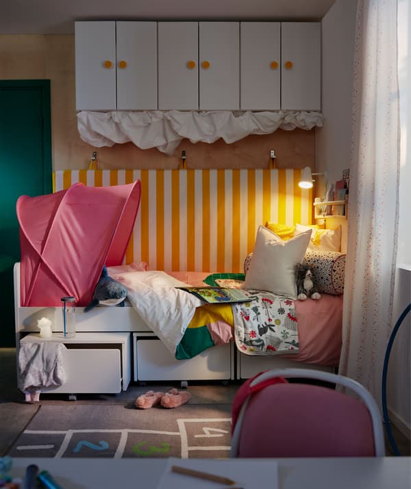 The bed corner of a child’s room, The bed has a mattress hung on the wall behind it, storage underneath and above.