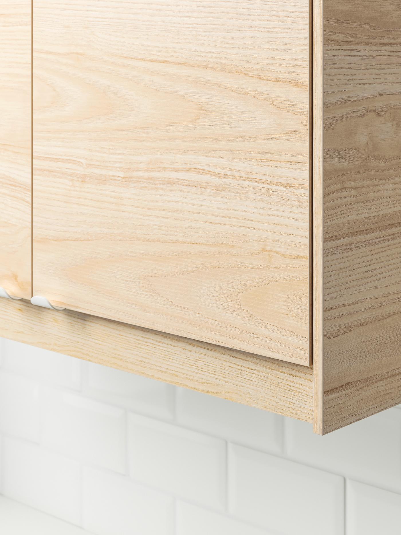The bottom corner of an IKEA SEKTION kitchen wall cabinet with an ASKERSUND light ash wood-effect front.