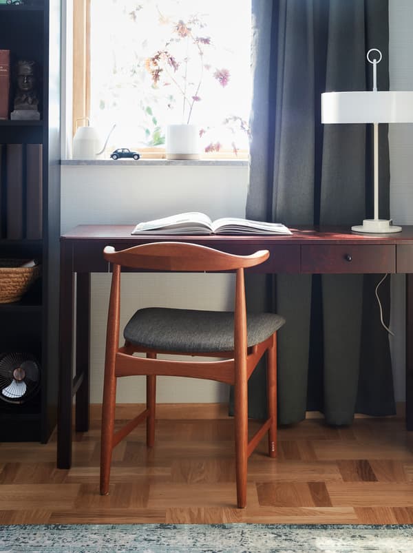 The chair DANSKE in oak with a textile seat designed for IKEA in the 60’s, standing in front of a desk in dark wood.