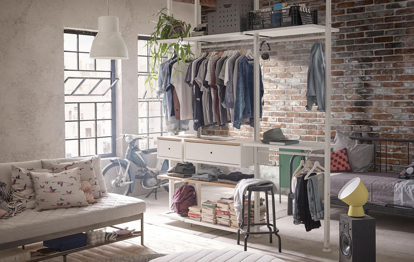 The ELVARLI storage system filled with clothing and books in a loft apartment featuring muted tones and exposed bricks.