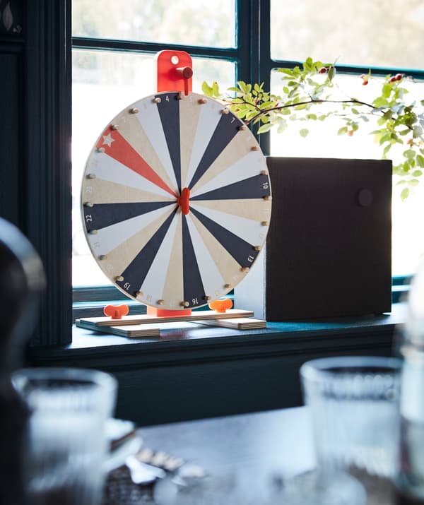 The IKEA LUSTIGT wheel of fortune game and ENEBY bluetooth speaker in a window sill.