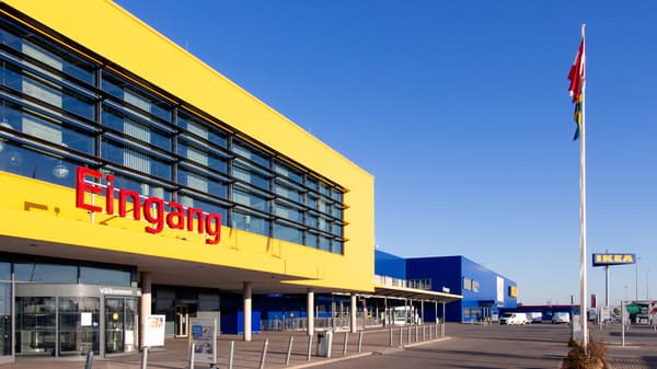 The image shows the entrance area of an IKEA store with a glass facade, a yellow canopy, and the word 