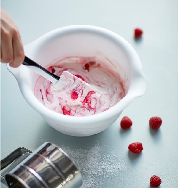 The ingredients for raspberry frozen yogurt are stirred together in a bowl.