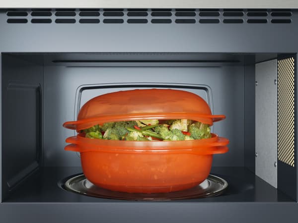 The inside of a microwave with an orange plastic bowl filled with veggies.