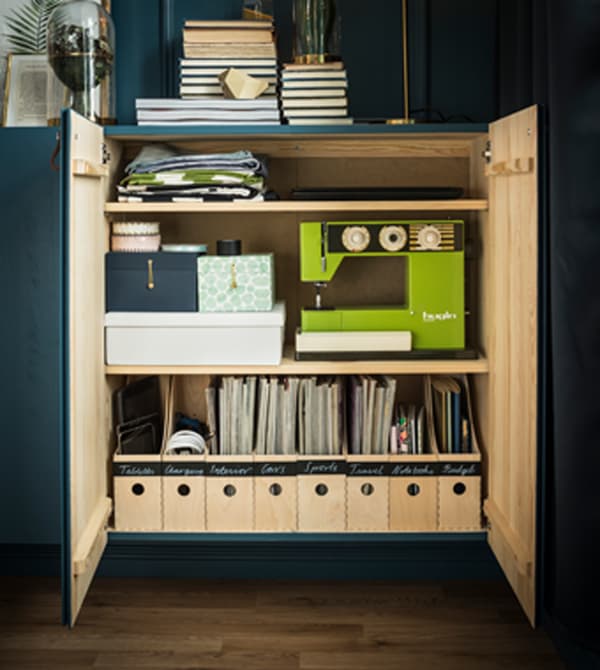The inside of an cabinet is arranged to organise magazines, a sewing machine, and various other items.