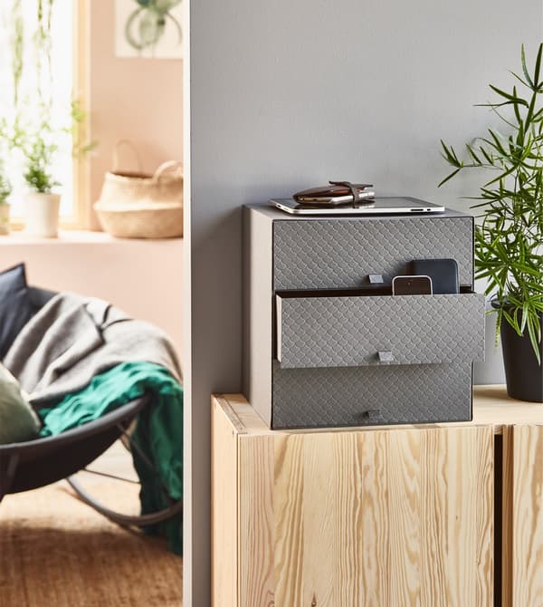 The mini chest PALLRA in dark grey sitting on a wooden cabinet.