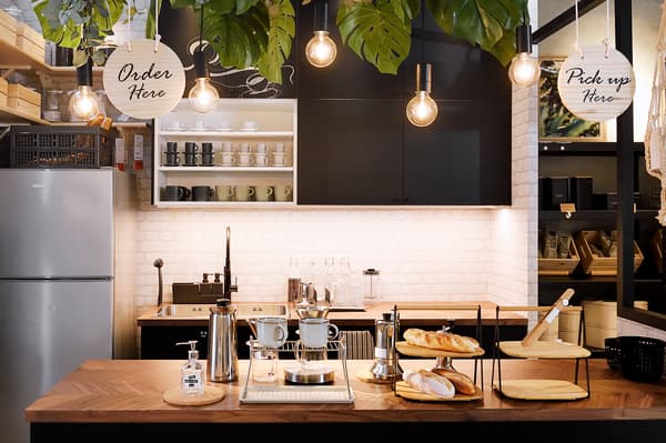 The ordering area of the café featuring a wooden countertop with coffee jugs and bread.