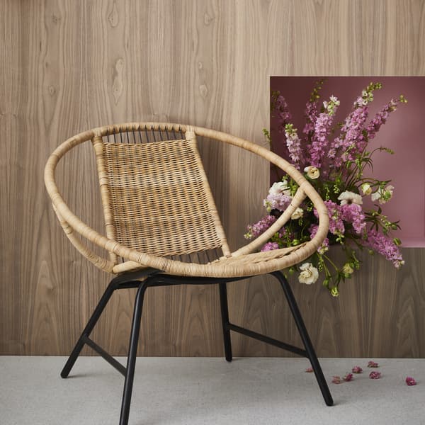The rattan GAGNET armchair next to some pink flowers.