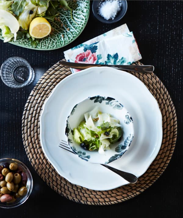 The round IKEA LÄTTAD seagrass place mat on a black dining table with white and floral dishes.