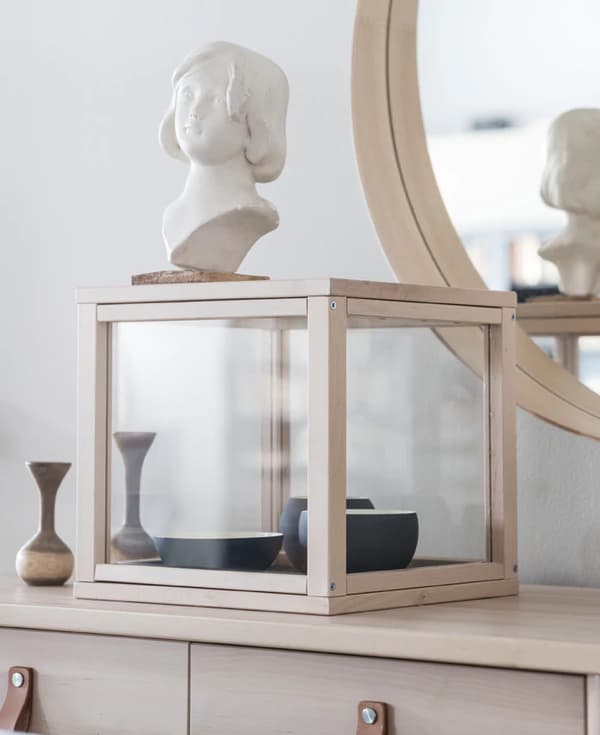 The SAMMANHANG display box used to display a collection of black ceramic bowls and decor on a blond wood dresser.