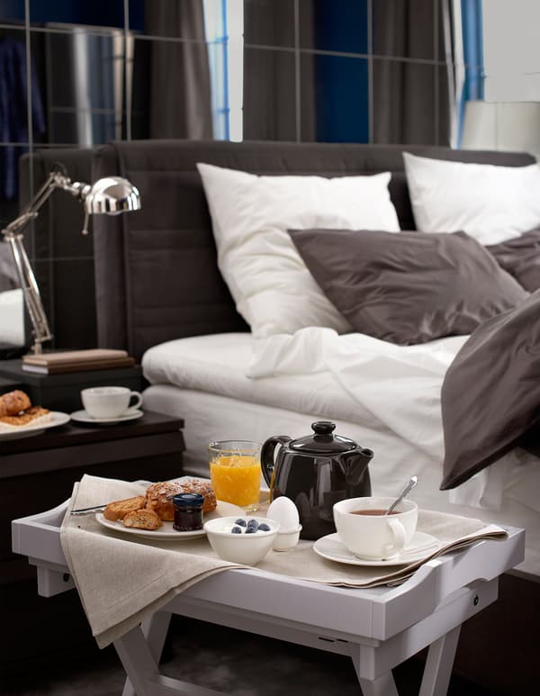 The side of a bed and tray table with breakfast.