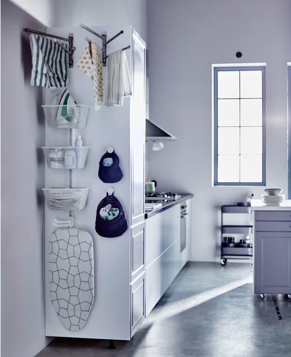 The side of a tall kitchen cabinet with baskets and rails for a laundry station.