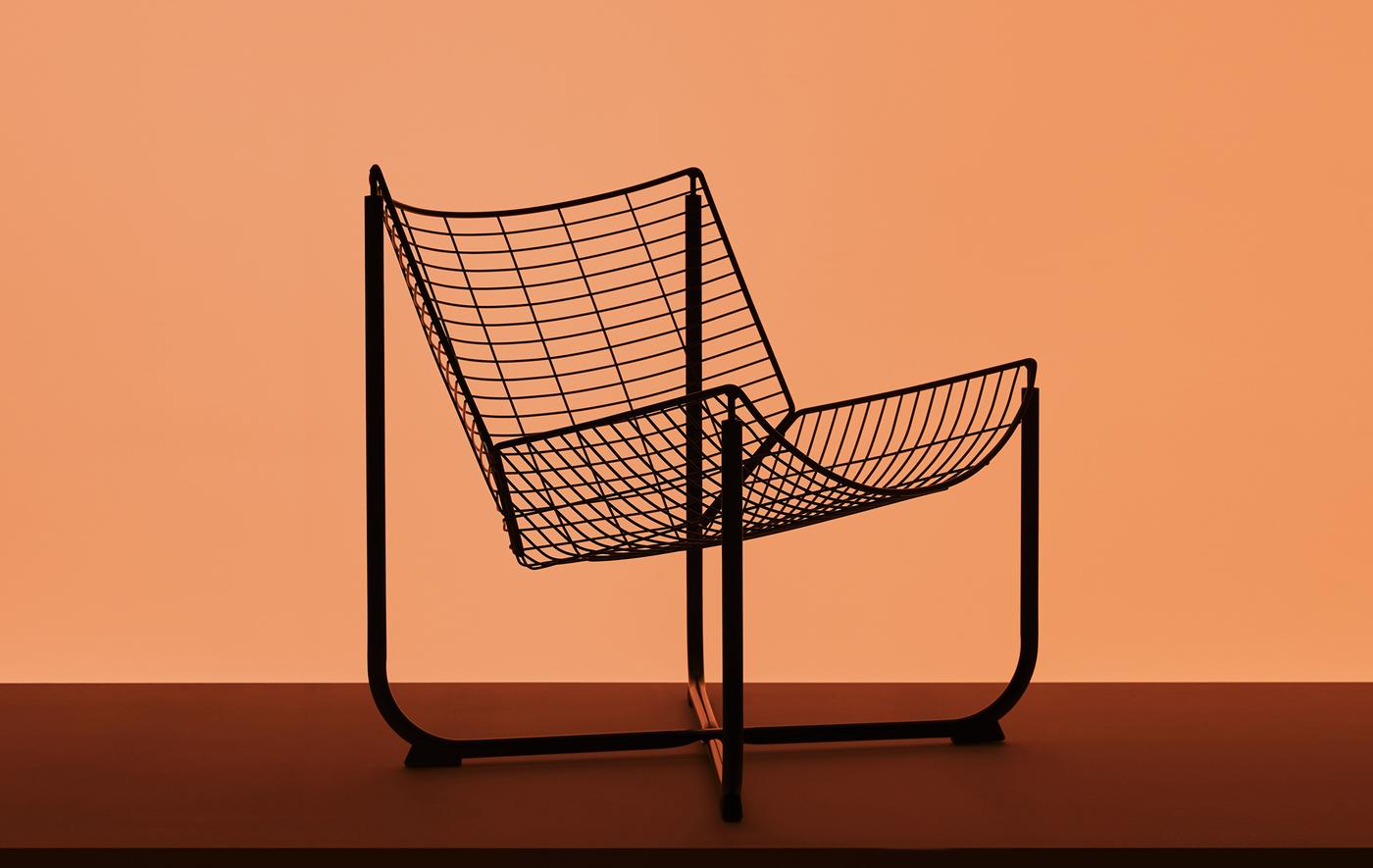 The silhouette of a black wire armchair against an orange backdrop.