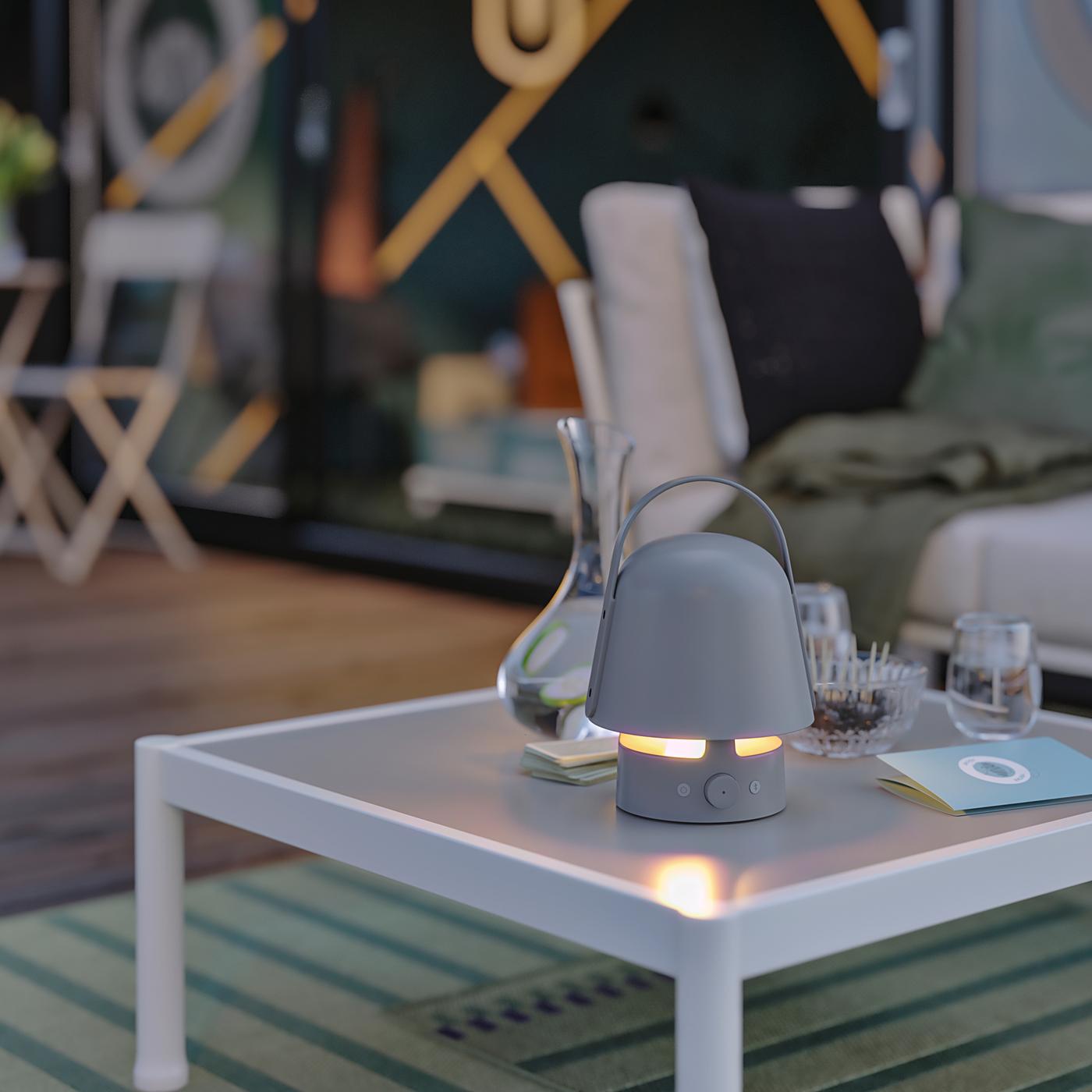 The sun is setting on an outdoor area. There is a lit VAPPEBY bluetooth speaker lamp on a SEGERÖN coffee table.