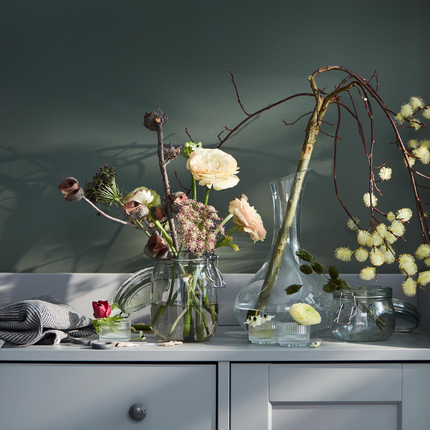 The top of a grey HAUGA sideboard is filled with various vase-and-flower combinations, one including a STORSINT carafe.