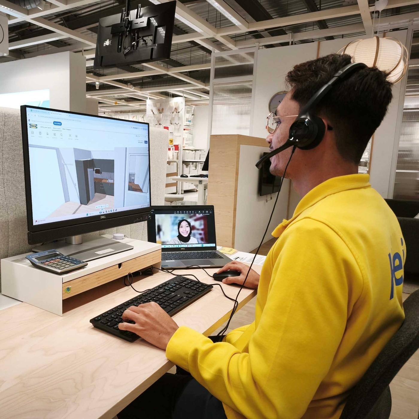 The visual shows an IKEA co-worker wearing a yellow IKEA shirt and a headset, using a computer to assist a customer with a 3D furniture planning design in an IKEA store.