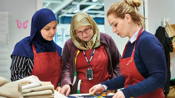  ثلاث لاجئات يقدمن خدمات الخياطة للعملاء في أحد معارض ايكيا ينظرن إلى نقش أحد اللمنسوجات سويًا.