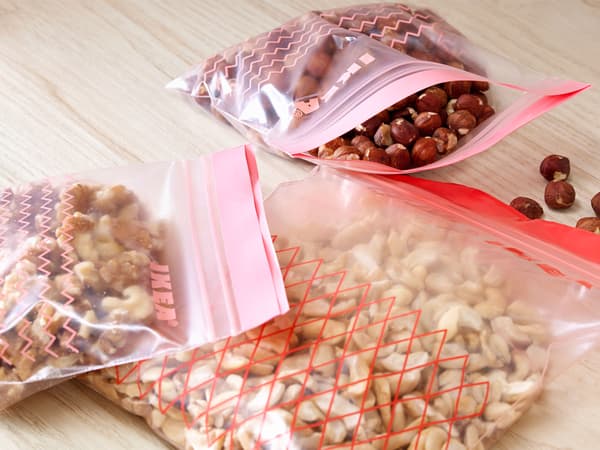 Three ISTAD plastic bags containing different kinds of nuts on a wooden worktop.