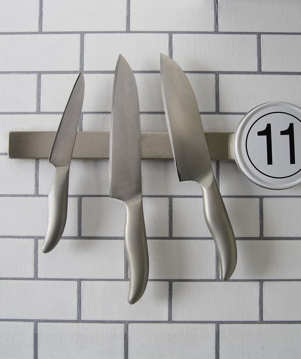 Three knives hang on a magnetic rail on a tiled wall.