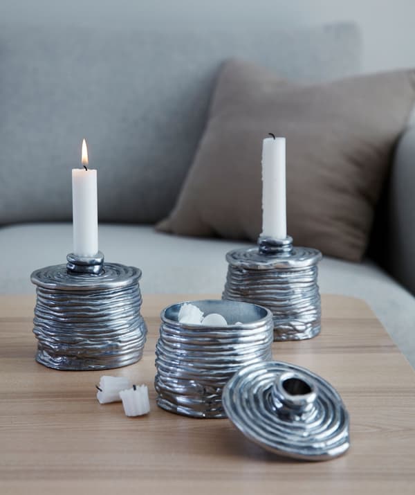Three metallic candleholders, two with candles and the third – demonstrating that it’s also a small box – with the lid off.