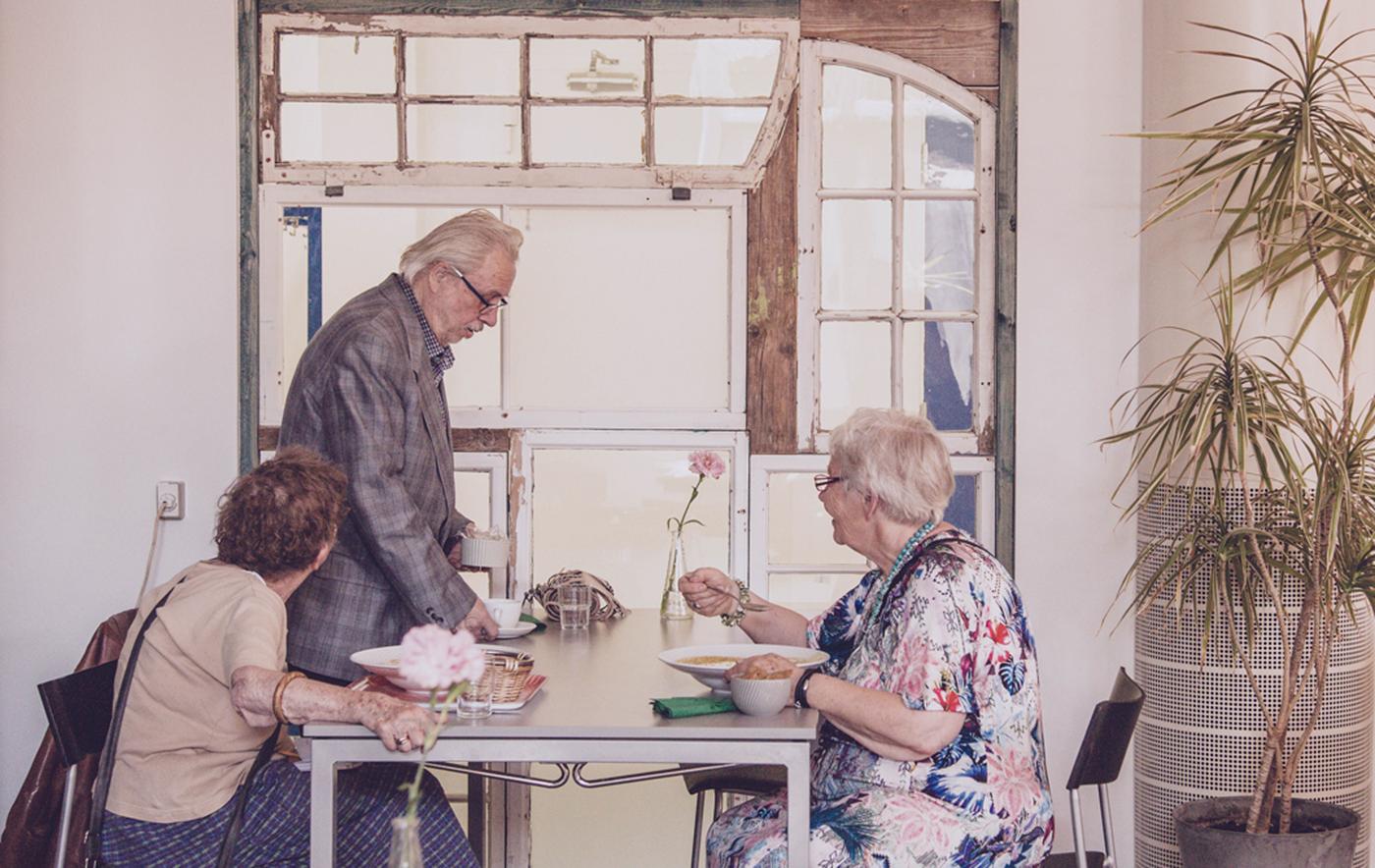 Three older people sit at a table eating a meal together.