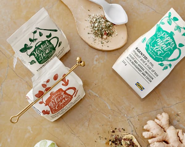 Three packages of IKEA EGENTID teas surrounded by herbs and spices used to give them their flavours.