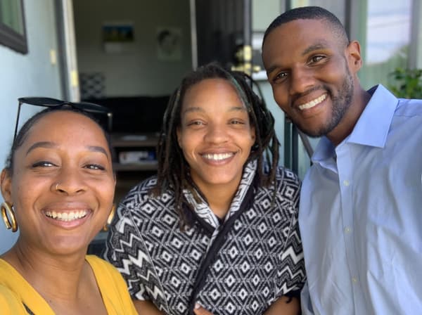 Three people are huddling together and smiling to pose for a photo in their home.
