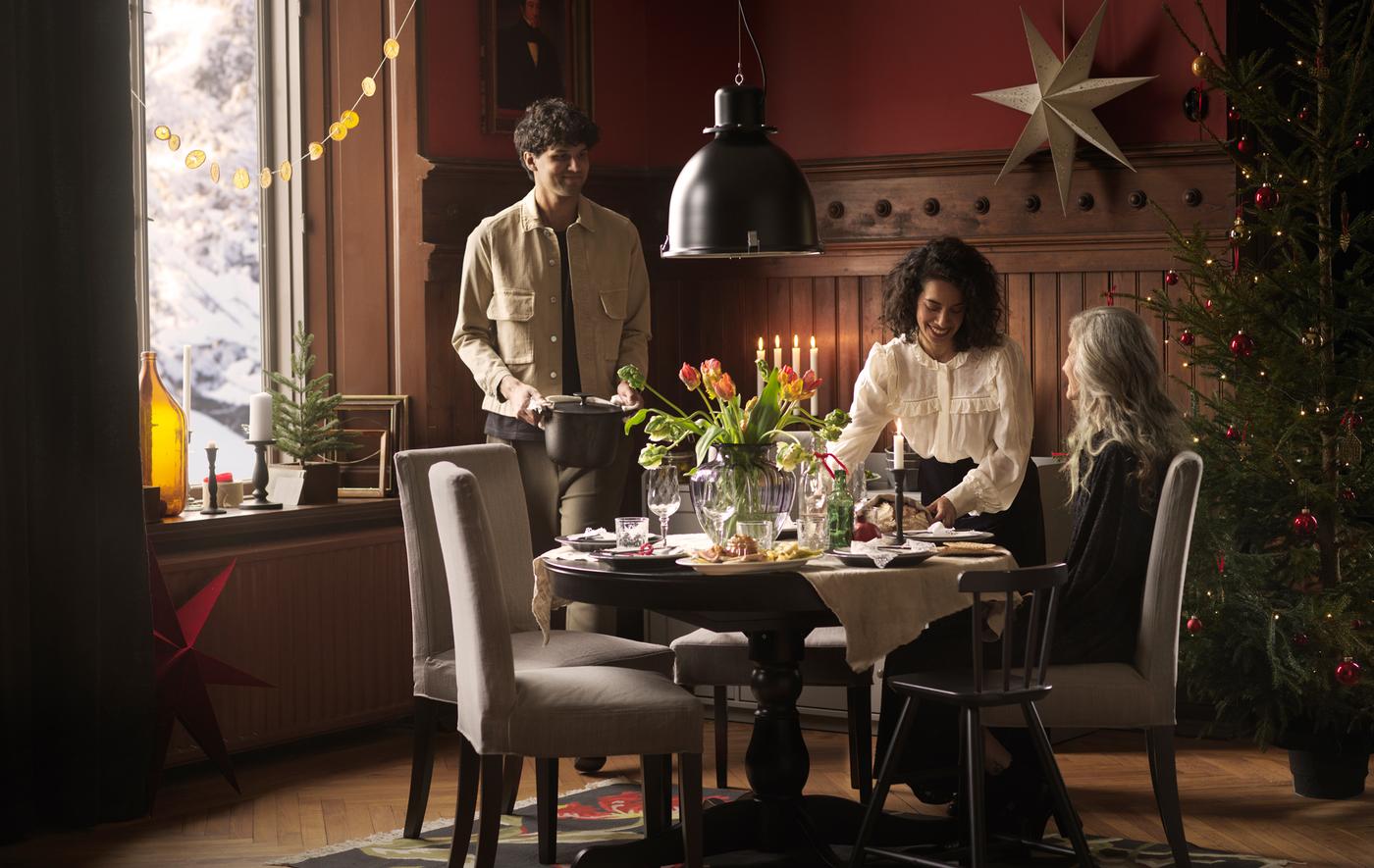 Three people gather round a round INGATORP table decorated with fresh flowers to eat a holiday meal together.