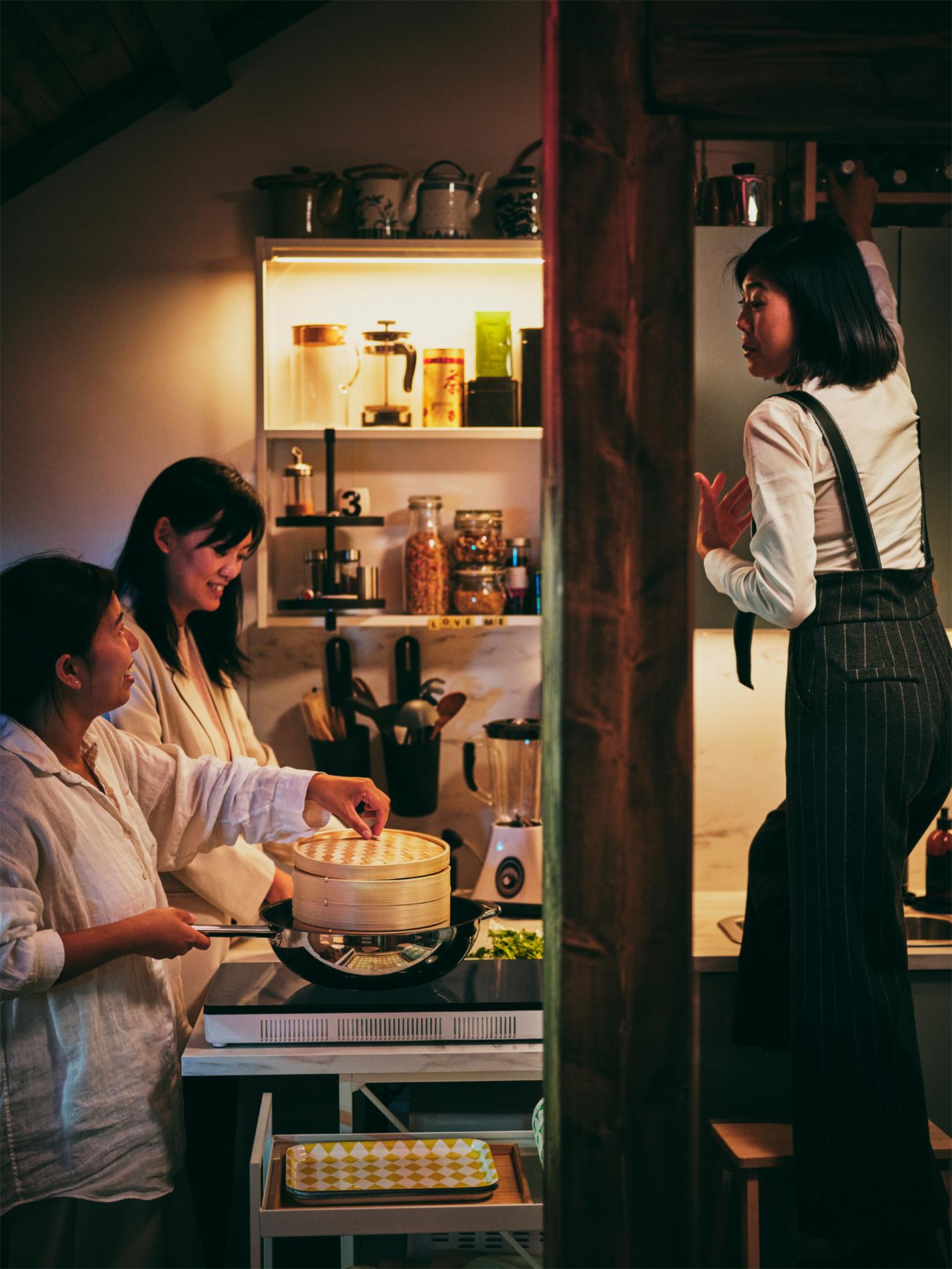 Three people in a kitchen with one person steaming food over an IKEA 365+ wok on a TILLDREDA portable induction hob.