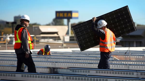 Three people working on installing solar panels with IKEA logo at the back
