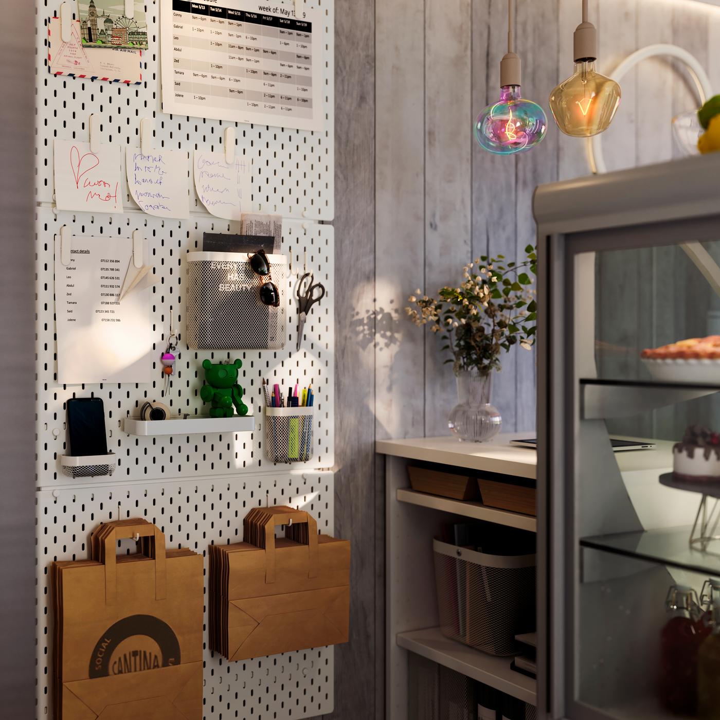 Three SKÅDIS pegboards are mounted on the wall next to the counter in a café. There are shopping bags hanging from hooks.