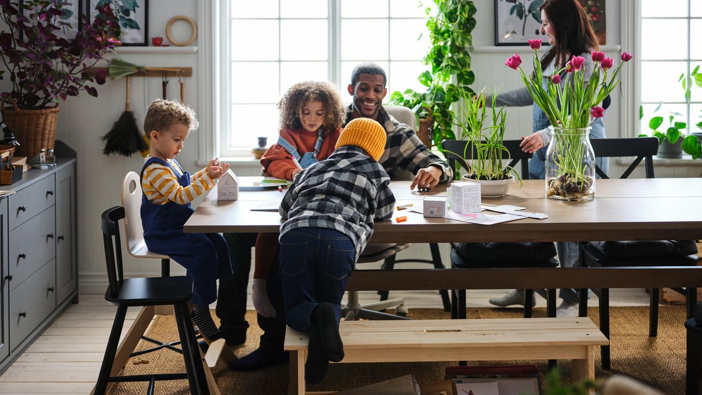 Three small children and their parents go happily about their business in a dining area with a grey-brown KLIMPFJÄLL table.