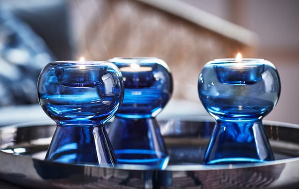 Three tealight holders made of blue glass on a silver tray.